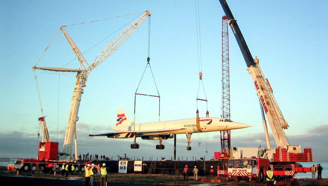 Two Bay Crane cranes performing a tandem lift of a retired Concorde aircraft at golden hour
