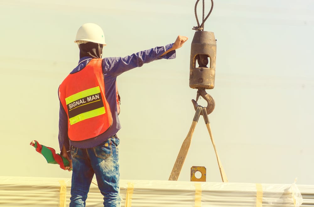 A qualified signal person in a high-visibility vest directing a crane lift